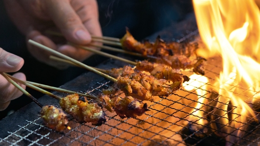 skewers of lab-grown chicken being cooked on a flaming grill
