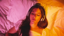 a female-presenting person wearing headphones while lying in bed. her eyes are closed.