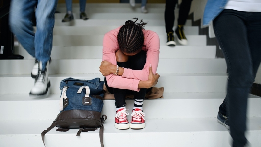 a girl with depression sitting on the stairs with her backpack.